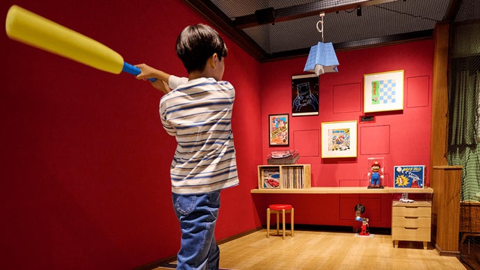 A Nintendo Museum guest swinging a foam bat in a recreation of a Japanese home as an Ultra Machine DX pitching machine fires out balls.