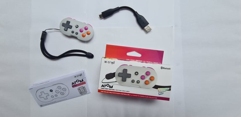 A picture  of the unboxed CRKD Atom, a small game controller, with surrounding accessories