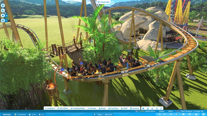 Planet Coaster 2 screenshot showing a rollercoaster cart tearing along a track as it whips up from beneath a wooden bridge surrounded by trees.