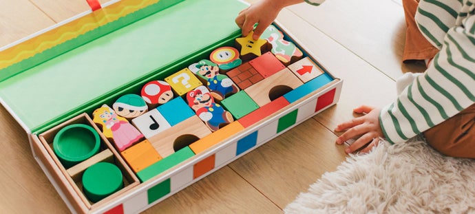 Promotional photo showing a young child reaching into a large box containing Mario-themed wooden blocks.